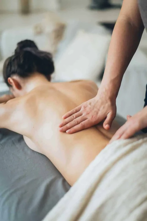 Massage - Frau liegt auf der Massageliege und wird am unteren Rücken sanft massiert. Es schaut sehr entspanned und schmerzlindernd aus. 